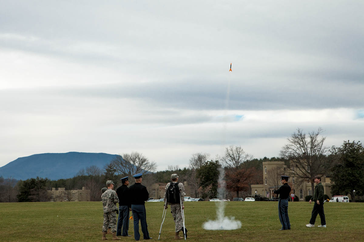 The quad at VMI. A group of students are launching bottle rockets. In the background is House Mountain.
